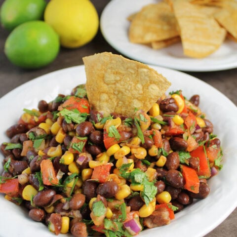 white bowl of black bean and corn salsa with a chip dipped