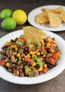 white bowl of black bean and corn salsa with a chip dipped