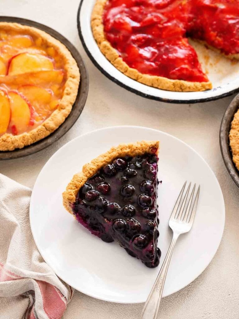 peach pie, strawberry pie, and a slice of blueberry pie on a white plate with a fork.