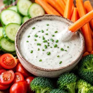 dairy-free ranch dressing in a bowl surrounded by carrots, cucumbers, broccoli, and tomatoes.