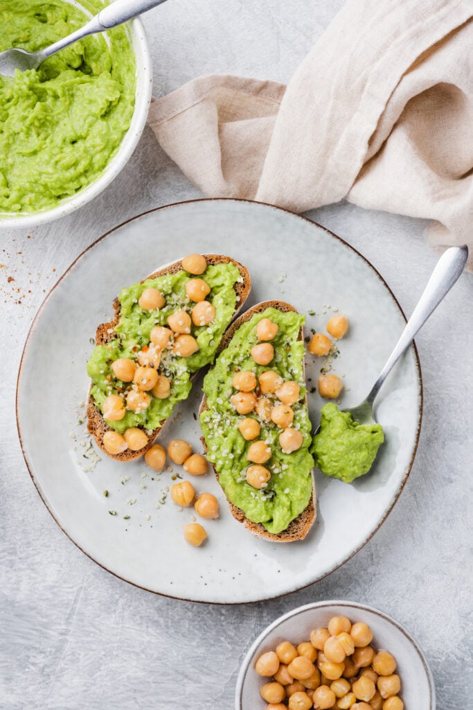 2 slices of avocado toast on white plate topped with chickpeas