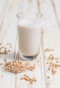glass of soy milk on white background with soybeans scattered around