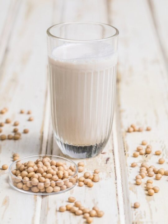 glass of soy milk on white background with soybeans scattered around