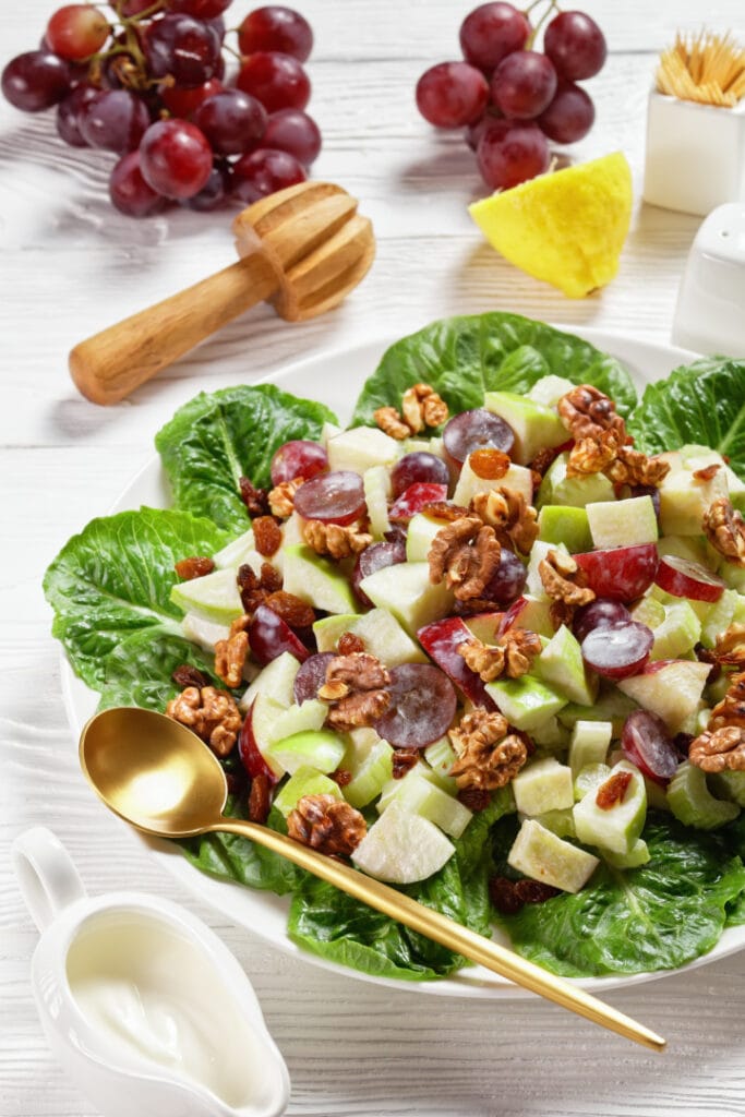 Waldorf salad with red grapes, celery, fresh green apple, walnuts, raisins on a pad of fresh lettuce leaves on a white plate on a wooden table, vertical view