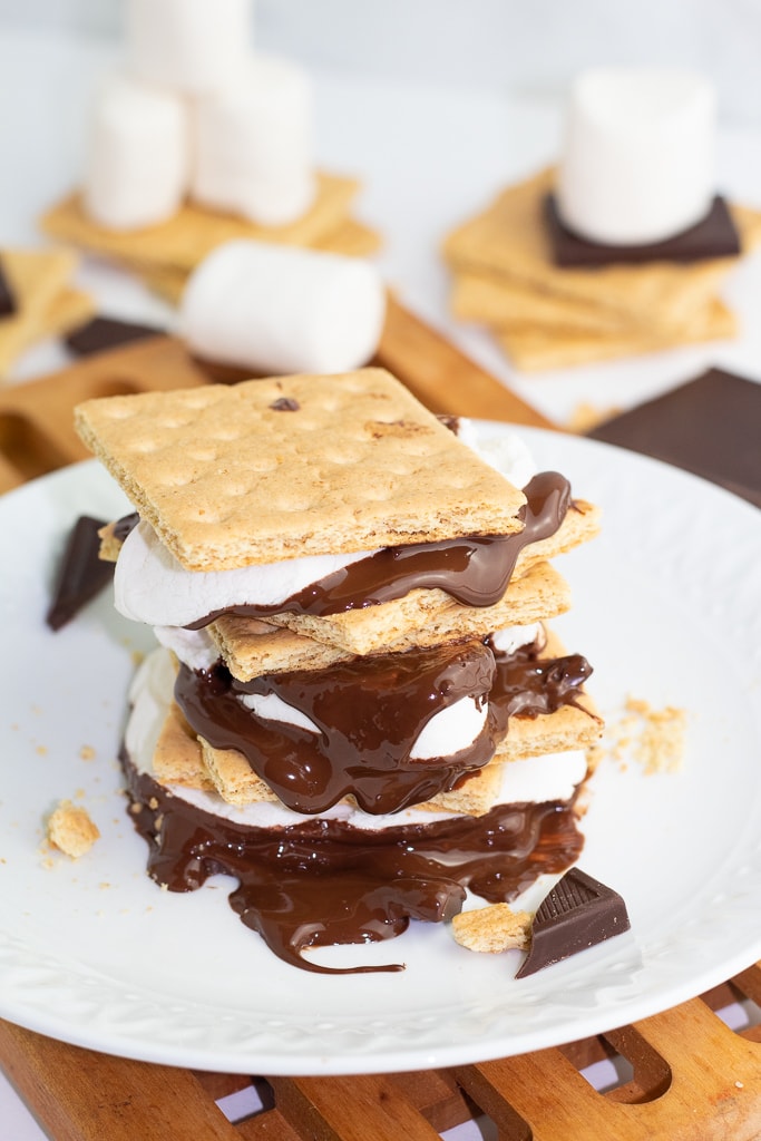 3 s'mores stacked high with chocolate, marshmallows, and graham crackers on white plate
