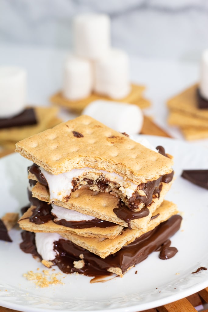 s'mores stacked on white plate with one bite out of top