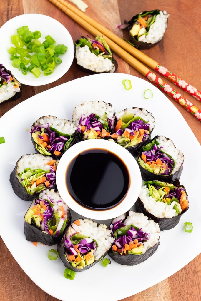 white plate of colorful vegan sushi on wooden board with chopsticks