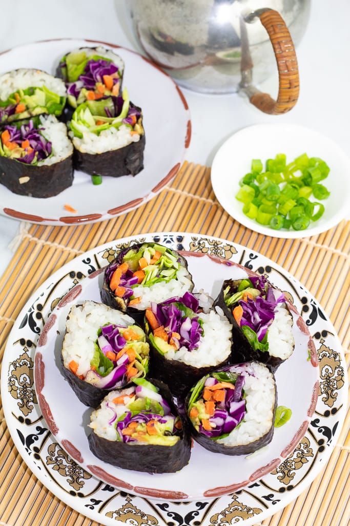 overhead photo of pieces of veggie sushi on Japanese plate and setting on a rice mat