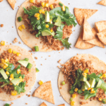 overhead shot of cauliflower tacos with corn tortillas, cilantro, and lime on white background