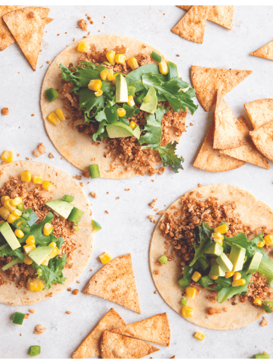 overhead shot of cauliflower tacos with corn tortillas, cilantro, and lime on white background