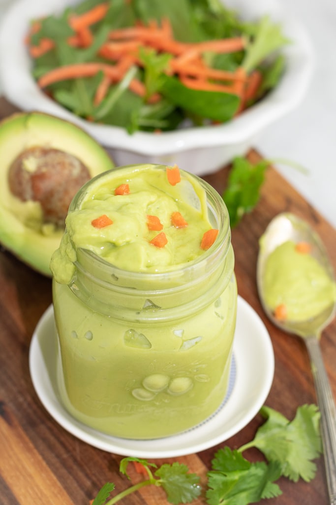 small mason jar of cilantro lime dressing sitting on a wooden board with salad in the background