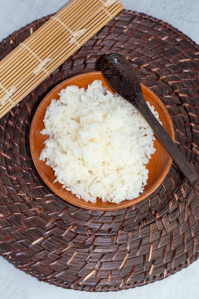 sushi rice in round wooden bowl on asian mat with bamboo rolling mat and spoon