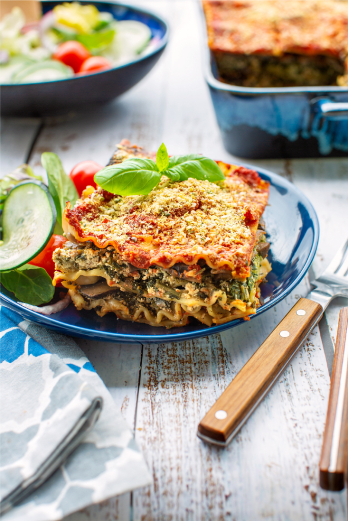 vegetable lasagna recipe on dark blue plate on white wooden table with fork