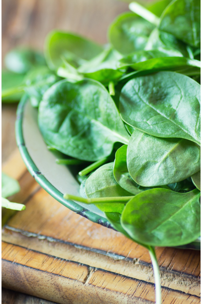 baby raw spinach leaves on plate on wood table