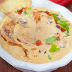 corn chip being dipped into vegan queso in white dish