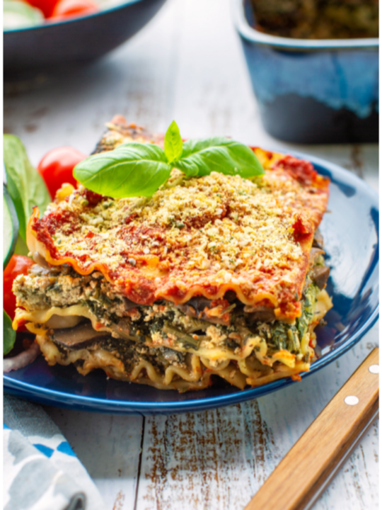 vegetable lasagna with spinach on blue plate with salad