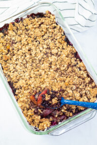 glass baking dish filled with blueberry peach crisp and country blue serving spoon