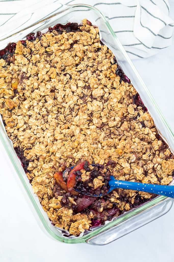 glass baking dish filled with blueberry peach crisp and country blue serving spoon
