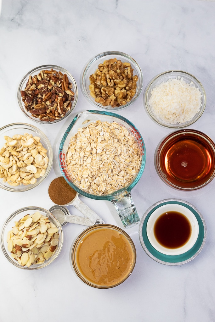 ingredients for granola on white background: gluten free oats, maple syrup, peanut butter, nuts, vanilla
