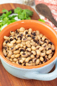 blue and orange crock bowl with cooked instant pot black eyed peas on a board