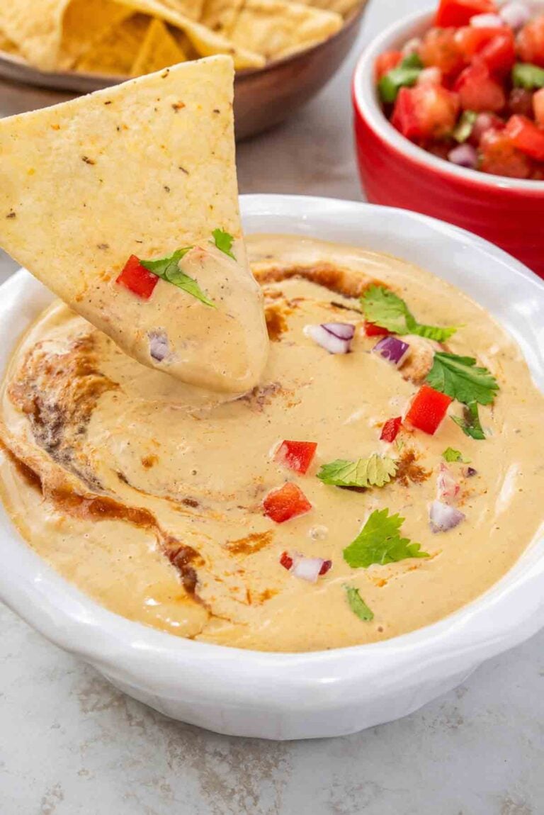 cashew queso in a white bowl with a dipped corn chip.