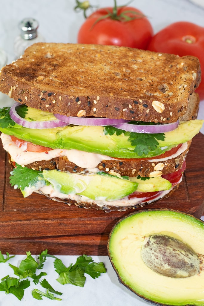 close up of healthy avocado sandwich on a cutting board with half of an avocado in front