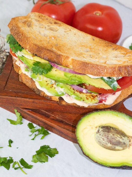 avocado sandwich made with sourdough toasted bread on white background with half of an avocado on