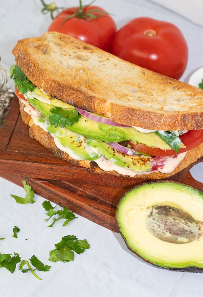 avocado sandwich made with sourdough toasted bread on white background with half of an avocado on