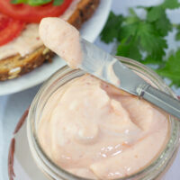glass jar filled with spicy vegan mayonnaise with knife and tomatoes