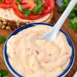 my spicy vegan mayo in a blue bowl with a spoon and sandwich in background.