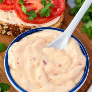 my spicy vegan mayo in a blue bowl with a spoon and sandwich in background.