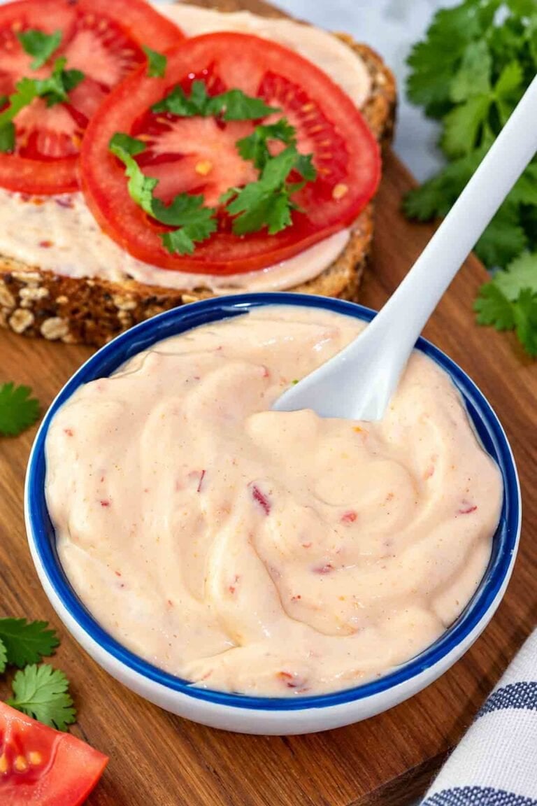 my spicy vegan mayo in a blue bowl with a spoon and sandwich in background.