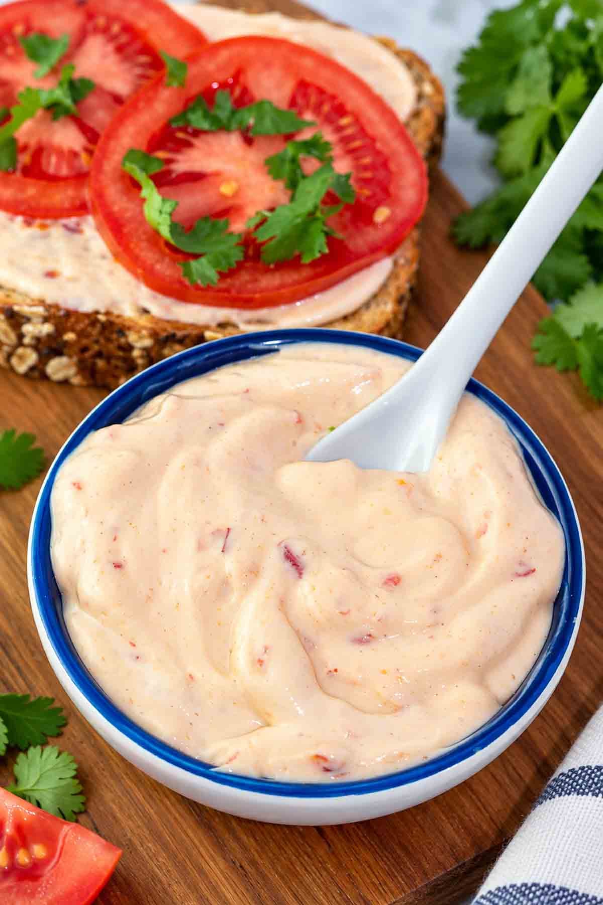 my spicy vegan mayo in a blue bowl with a spoon and sandwich in background.