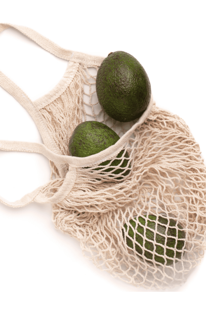 3 avocados in a net reuseable grocery bag on white background