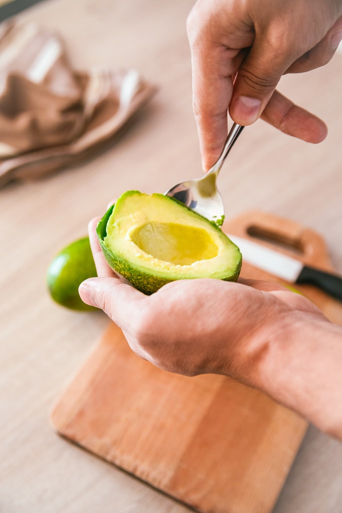 avocado being held in hands while scooping out flesh with spoon