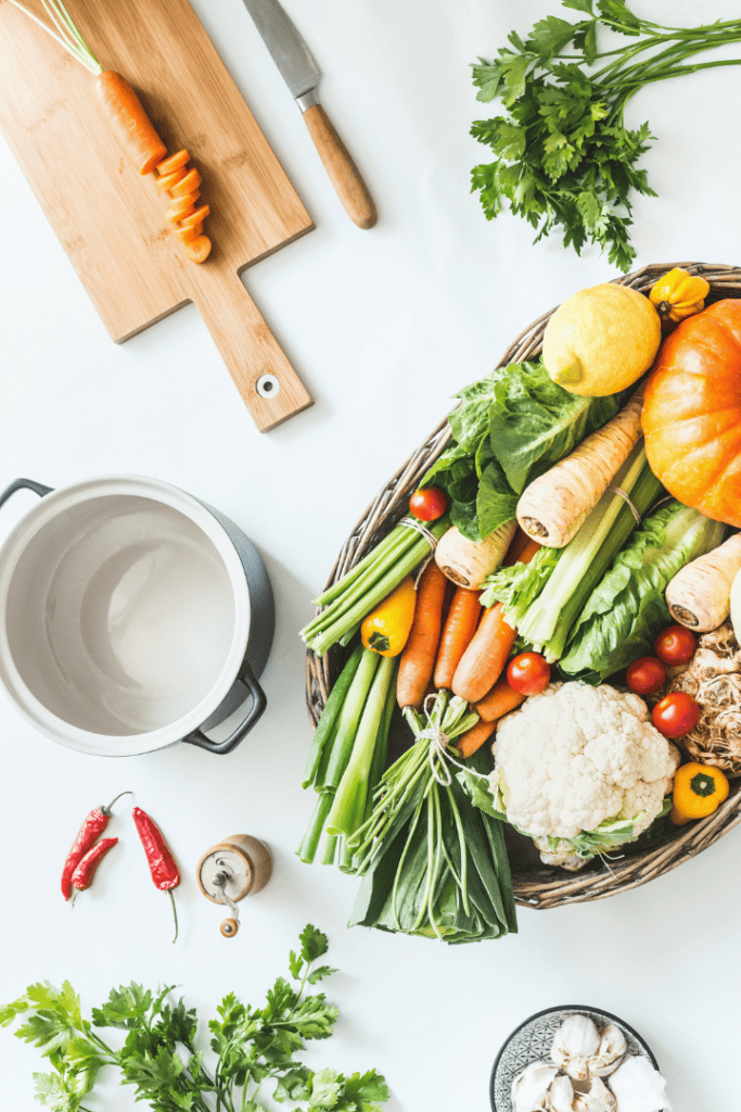 basket of vegetables on a white counter with a knife and stockpot
