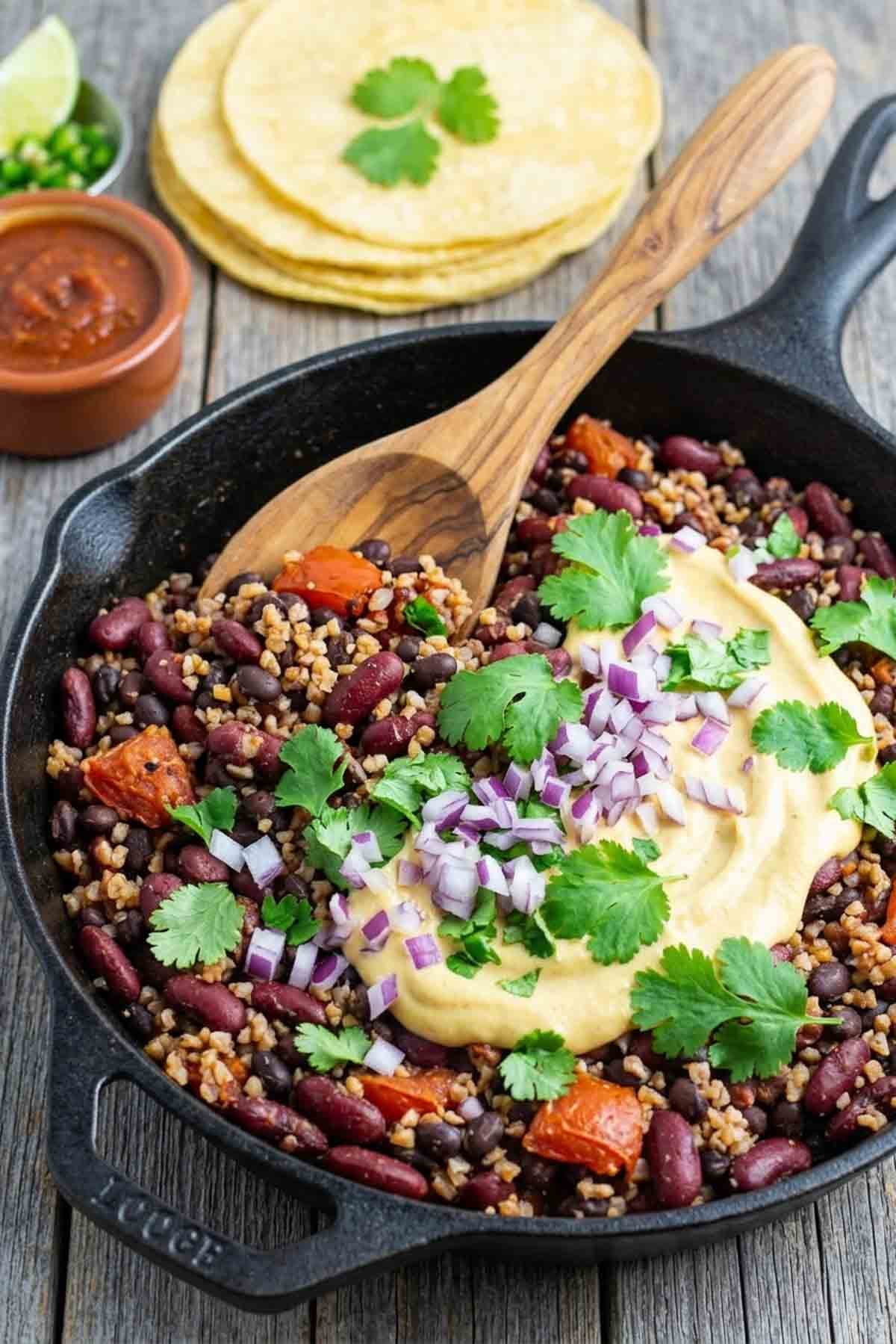 vegan bean bulgur filling in a pan with cashew cheese sauce and a spoon.