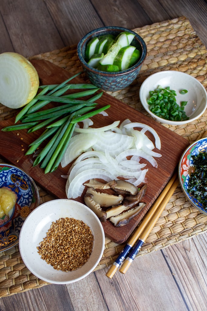sliced onions, chives, seaweed, and sesame seeds on cutting board with chopsticks