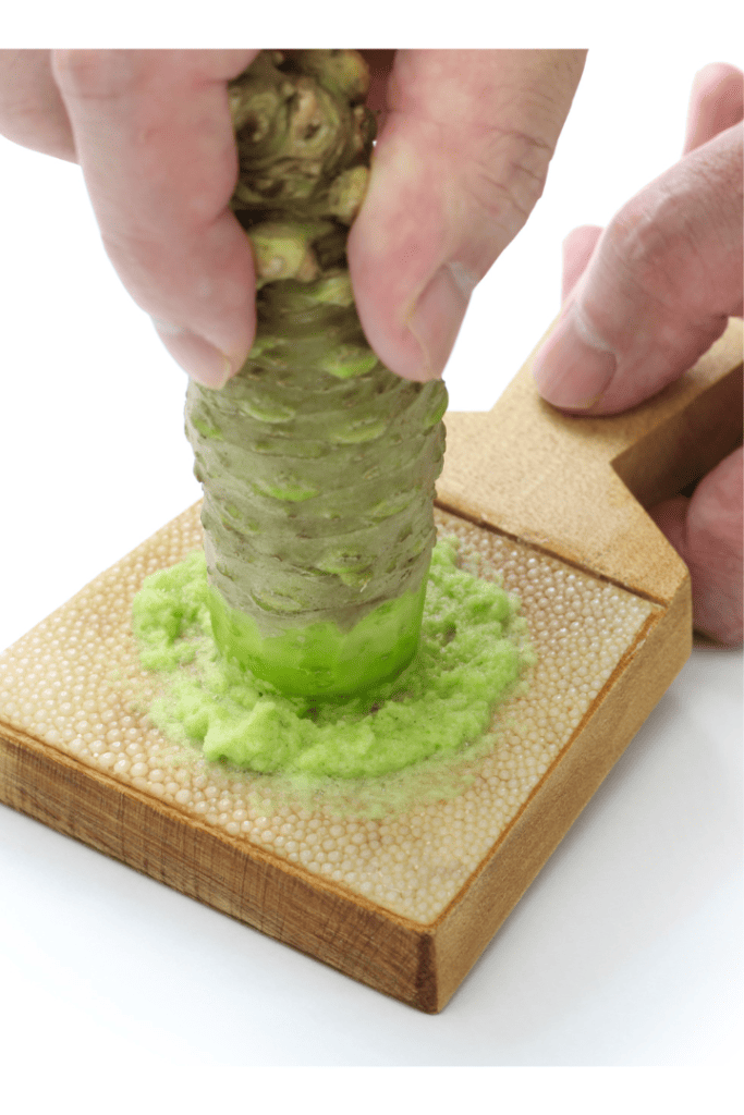 Wasabi plant being pressed with hands on cutting board