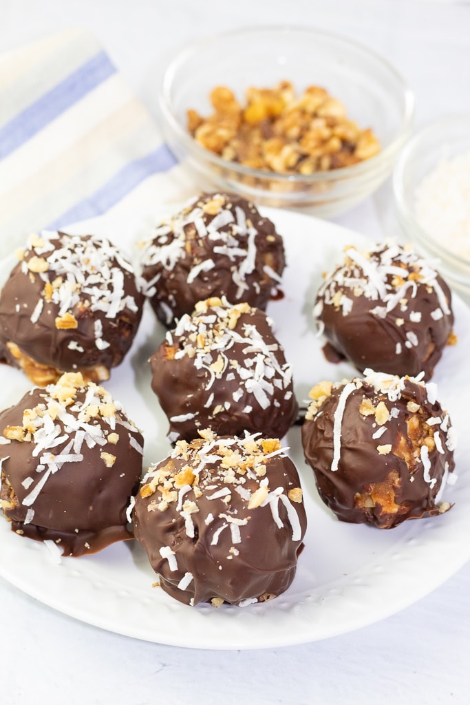 white plate with 7 chocolate balls sprinkled with shredded coconut and crushed walnuts