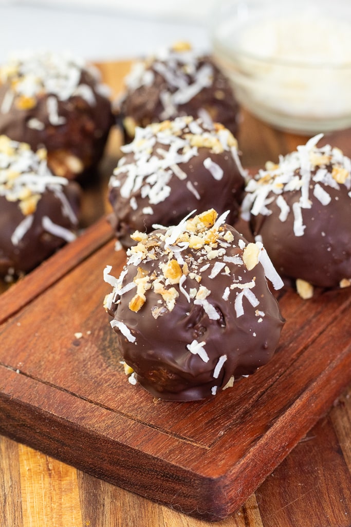 close of of 3 chocolate peanut butter balls on wooden boards with more balls in background