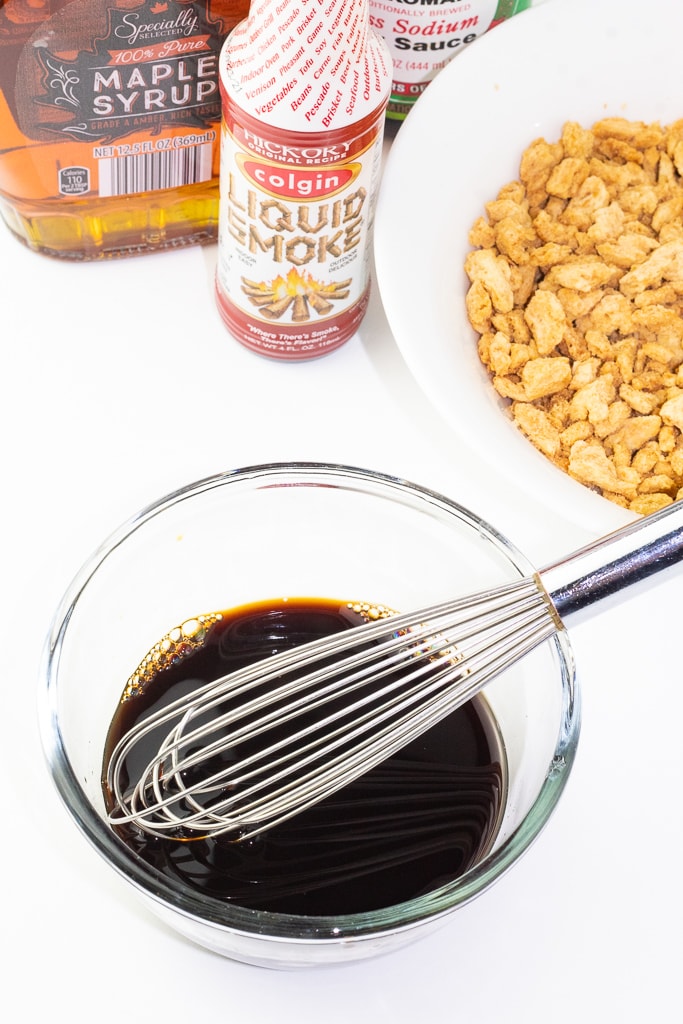 glass bowl filled with soy sauce, maple syrup, and liquid smoke with a stainless small whisk