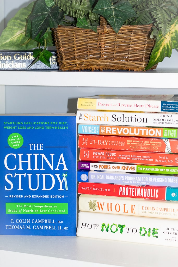 plant based books stacked on white book shelf with the china study standing up