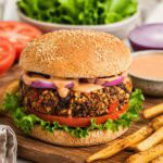thick vegan black bean burger on a whole grain bun with lettuce, tomato, and chipotle sauce.