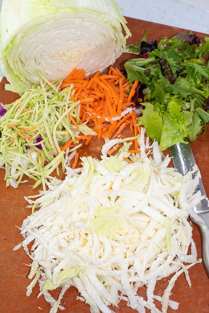 chopped napa cabbage, greens, and carrots on a cutting board