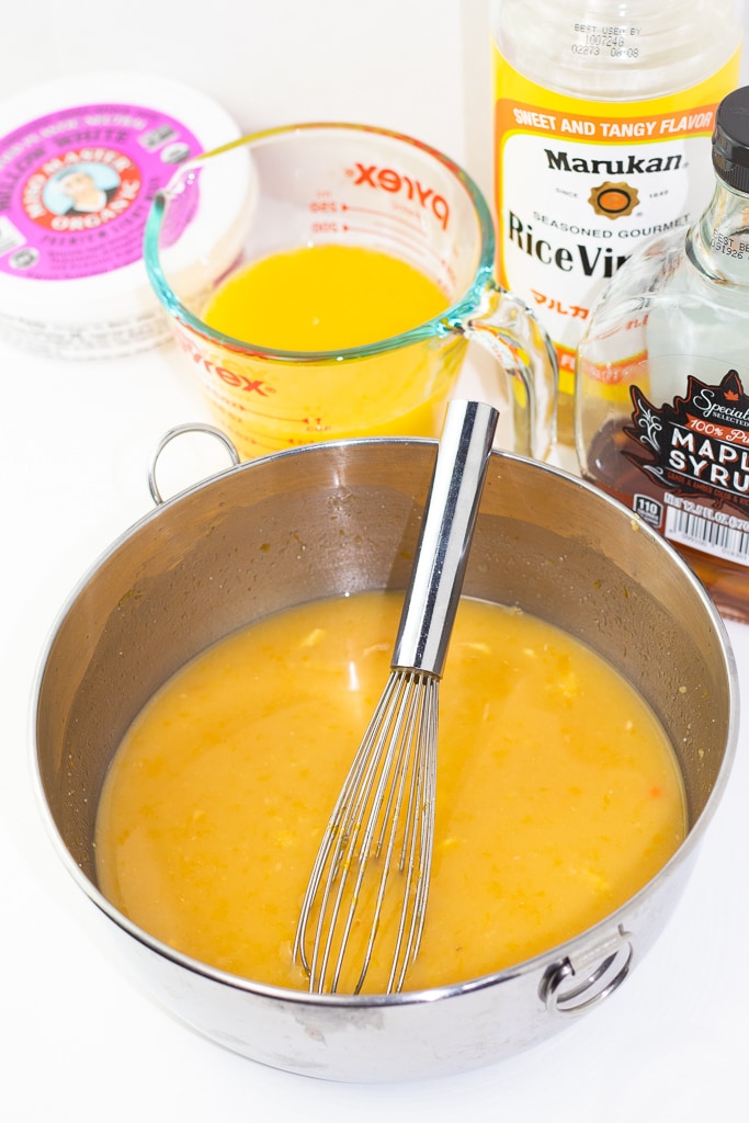 orange miso dressing in mixing bowl with whisk. orange juice, vinegar, maple syrup, and miso ingrients