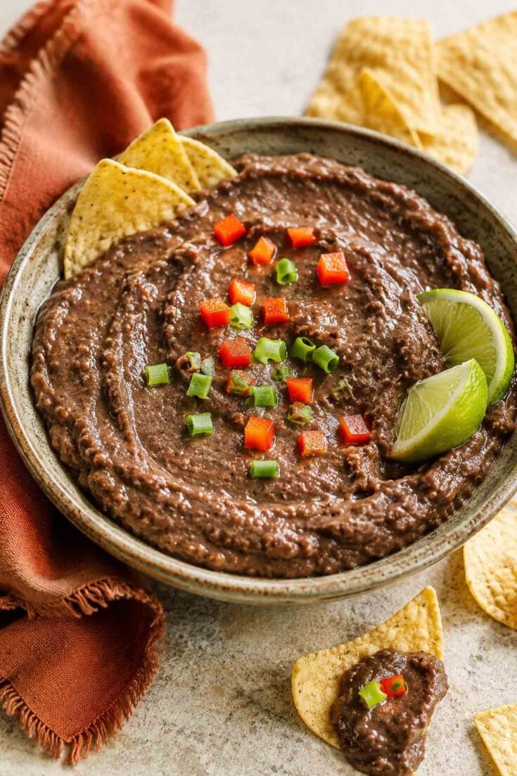 black bean dip in a rustic bowl with lime wedges and corn chips.
