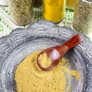 jars of spices around a dish with poultry seasoning blend and a measuring spoon