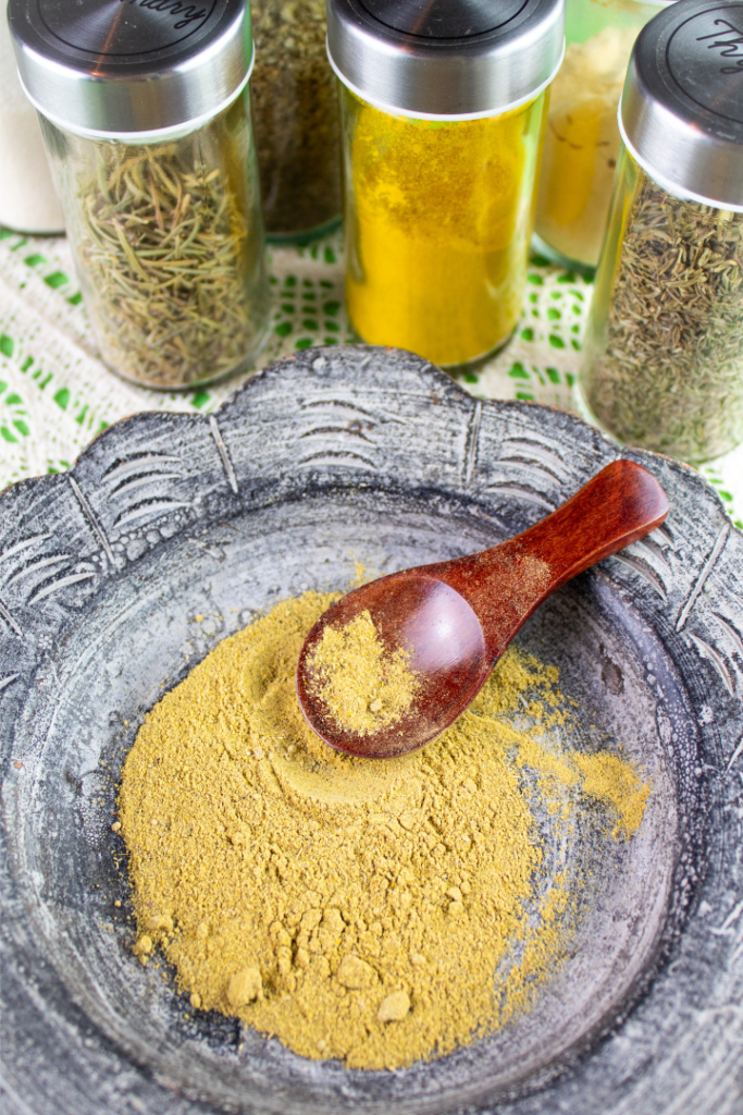 jars of spices around a dish with poultry seasoning blend and a measuring spoon