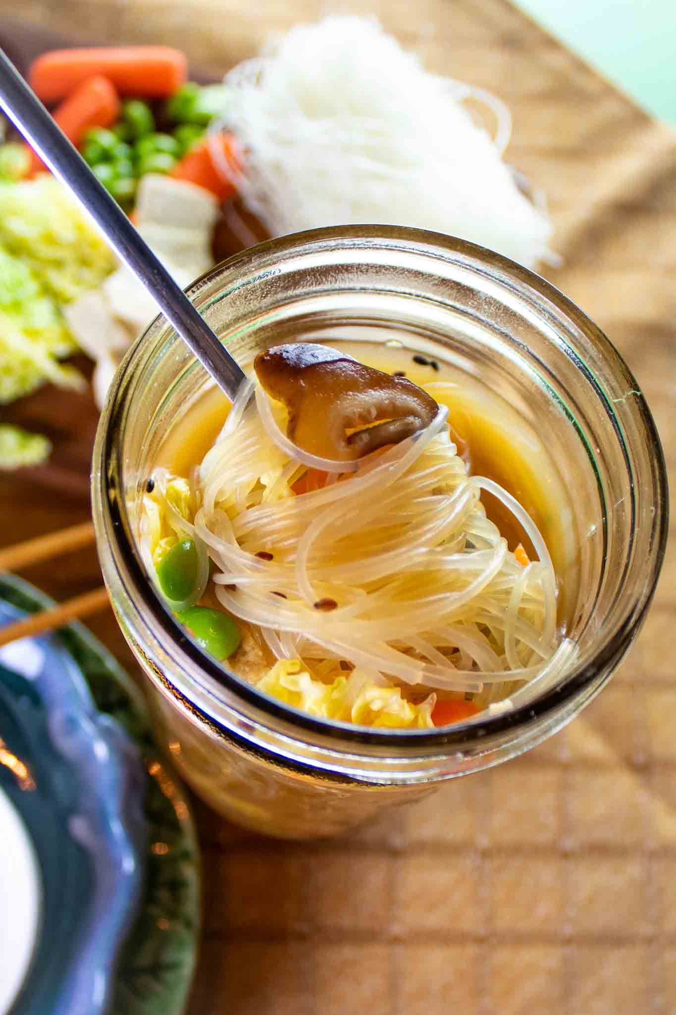 mason jar filled with asian noodle soup and vegetables with a spoon.